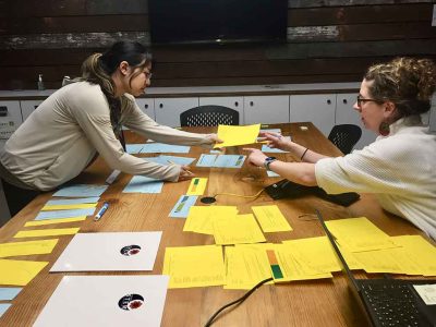 two women arrange pieces of paper over a table